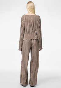 Haut plissé et pantalon à jambes larges dans une teinte de brun doux. Tissu texturé avec des bords en flûte sur les manches et l'ourlet, créant une silhouette fluide.