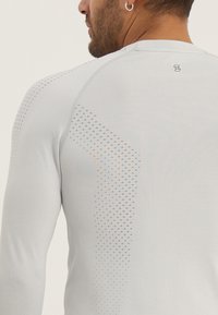 Helles graues Langarm-Sportshirt mit texturierten Akzenten und diagonalem Perforationsmuster auf dem Rücken. Verfügt über einen runden Ausschnitt.