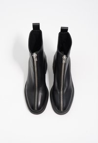 Botas negras de cuero hasta el tobillo con cremallera frontal, textura suave, puntera redonda y pestaña en la parte trasera para facilitar su colocación.