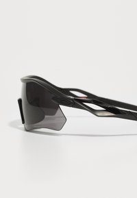 Black sports sunglasses with a wraparound design, gradient dark lenses, and sleek, lightweight frames featuring cut-out accents.