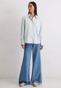 Világoskék-fehér csíkos gombos ing, széles szárú kék farmernadrággal párosítva. A lábbeli bézs talppal és világos díszítéssel rendelkezik.