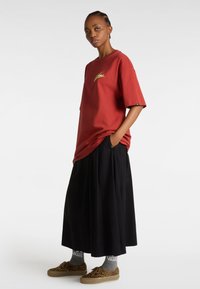 Camiseta de algodón roja con mangas cortas y gráfico en la parte delantera, combinada con falda negra con pliegues y zapatillas con estampado de leopardo, calcetines grises visibles.