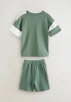 Groene katoenen t-shirt met witte accentmouwen, gedragen met bijpassende groene shorts met een elastische tailleband en een textuurstof.