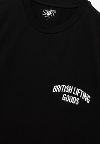 Camiseta de algodón negra con bordado en blanco que dice "BRITISH LIFTING GOODS", diseño de cuello redondo, textura suave y mangas cortas.