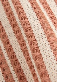 Textil med växlande ränder av mjuk persika och vitt med intrikata blommönster och spetsstruktur. Detaljerad, lager-på-lager design.