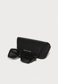 Ochelari de soare negri Michael Kors cu ramă pătrată și lentile colorate, așezați lângă o carcasă elegantă din piele neagră cu logo-ul mărcii.