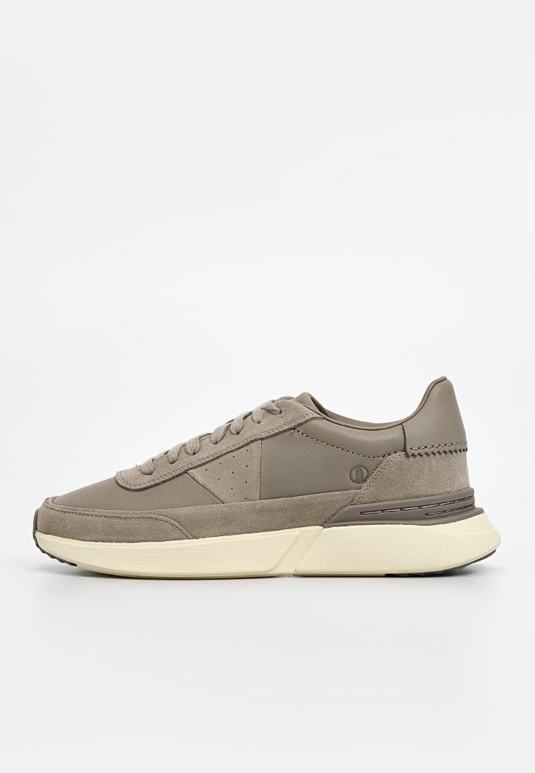 Scarpa sportiva grigia con una parte superiore in pelle liscia e dettagli in camoscio. Presenta una suola ammortizzata, una chiusura con lacci e un design minimalista.