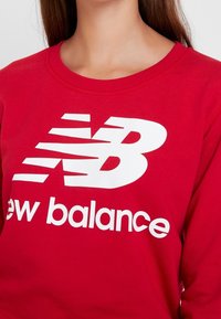 Felpa rossa a girocollo realizzata in cotone, con un grande logo bianco "New Balance" sul petto, in un carattere audace e elegante.