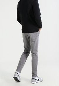 Pantaloni grigi a gamba stretta in tessuto misto cotone, abbinati a un maglione nero e sneakers bianche con dettagli neri.