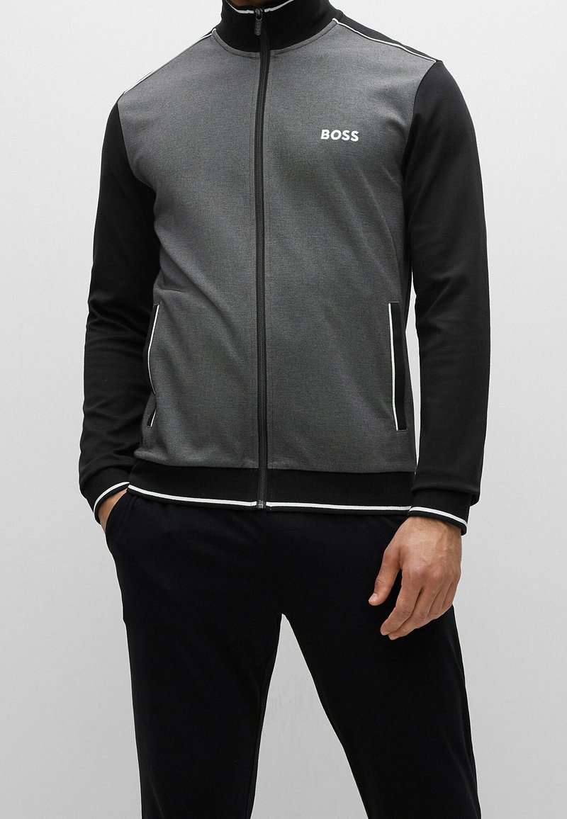 Giacca da track con zip nera e grigia, con colletto alto, dotata di un logo bianco e piping a contrasto lungo la zip e i polsini.