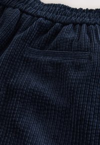 Tessuto in ciniglia blu navy con texture a coste verticali. Caratterizzato da una vita elasticizzata e una piccola tasca orizzontale.