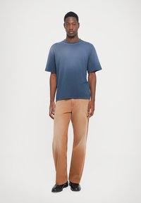 Modra majica s kratkimi rokavi in krožnim izrezom, v kombinaciji s svetlobrnimi širokimi hlačami. Črne čevlje dopolnjujejo komplet.