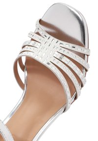 Sandalo con tacco alto argento, con tomaia metallici liscia, multiple cinghie bianche con piccole pietre di rhinestone, e suola beige.
