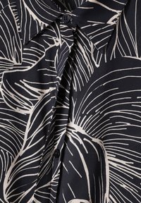 Chemise noire boutonnée avec de grands motifs abstraits de feuilles blanches et un col pointu.
