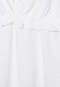 Tissu blanc avec un détail de couture froncée et volantée créant une texture et des ombres subtiles sur un matériau doux et fluide.
