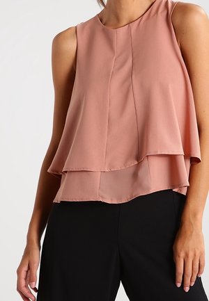 Bezrękawowa top warstwowy z miękkiego różowego materiału; ma okrągły dekolt i delikatne marszczenia na nachodzących warstwach.