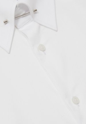 Col de chemise blanche avec renforts métalliques et deux boutons visibles sur un fond en tissu lisse.