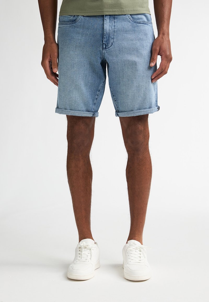 Pantalones cortos de mezclilla azul claro con dobladillos enrollados, que cuentan con bolsillos delanteros, una cintura de tiro medio y combinados con zapatillas blancas.
