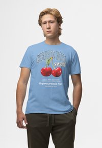Camiseta de algodón azul claro con un gráfico de cereza, con el texto "CHERRIE ROSA dulce" y "Productos orgánicos 100% CULTIVADOS EN ITALIA" en letras en negrita.