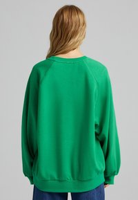 Zelená oversize mikina vyrobená z měkké tkaniny; má raglánové rukávy, kulatý výstřih a přiléhavý spodní lem. Texturovaný, ležérní design.