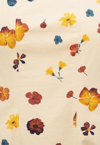 Ύφασμα σε κρεμ απόχρωση με διάσπαρτο μικρό λουλουδάτο σχέδιο σε κίτρινο, κόκκινο, μπλε και πορτοκαλί, με ορατές κάθετες ραφές.