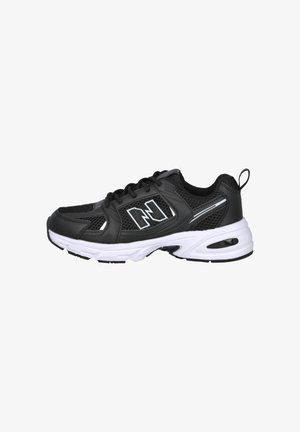 Zapatilla deportiva en blanco y negro con paneles de malla, cordones, cuello acolchado y suela blanca con detalles recortados.