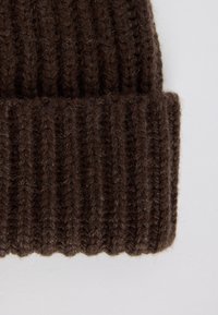 Berretto in maglia marrone scuro con texture a coste, caratterizzato da un risvolto e da un aspetto morbido e spesso.