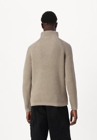 Beige Rippstrickpullover mit hohem Kragen und Raglanärmeln. Verfügt über ein strukturiertes Muster und eine taillierte Silhouette.