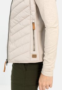 Helle beige gesteppten Weste mit einer Reißverschlusstasche, aus weichem Material gefertigt. Verfügt über kontrastierende gerippte Ärmel und ein kleines braunes Logopatch.