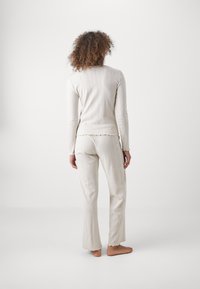 Helle beige gerippte Freizeitkleidung bestehend aus einem Langarmoberteil mit gewellten Kanten und passenden Hosen. Weicher Textil, lockere Passform.