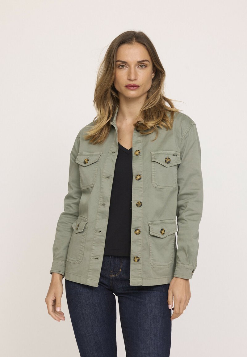 Veste utilitaire vert olive avec boutons sur le devant, quatre poches et manches longues. Fabriquée en coton, elle présente une texture lisse et un design léger.