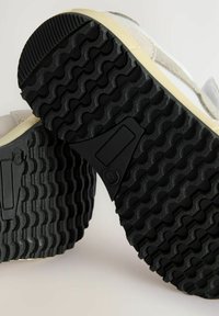 Zwarte rubberen zool met zigzag profiel, voorzien van een beige buitenlaag en een gestructureerde, suede-achtige accent. Minimalistisch ontwerp.