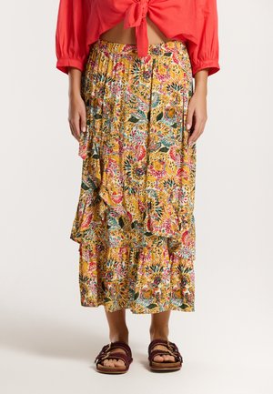 Gonna maxi floreale con base gialla, caratterizzata da strati arricciati e motivi multicolori. Accoppiata con sandali scuri.