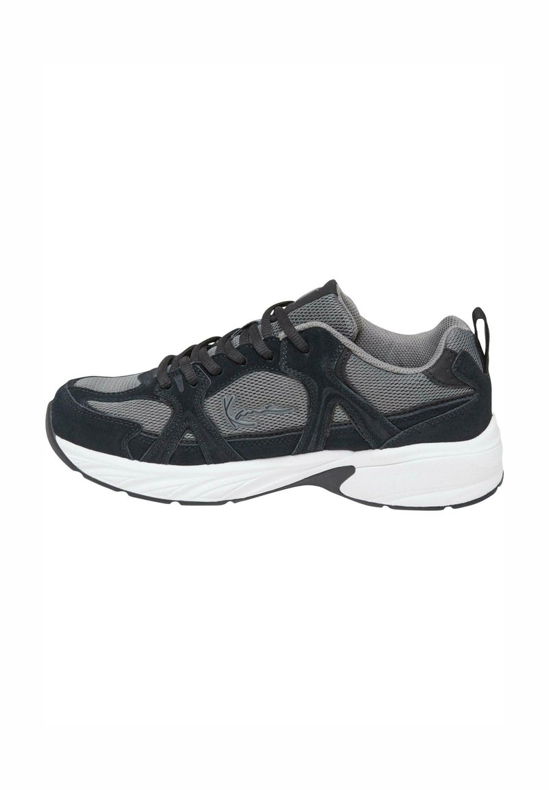 Chaussures de sport noires et grises avec dessus en mailles et en suédine, semelle intermédiaire blanche et semelle extérieure noire. Comprend des lacets et une languette à l'arrière.