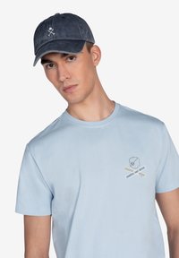Gorra de color azul marino oscuro con visera curva y logo bordado. Camiseta de cuello redondo en azul claro con un pequeño diseño bordado en el pecho.