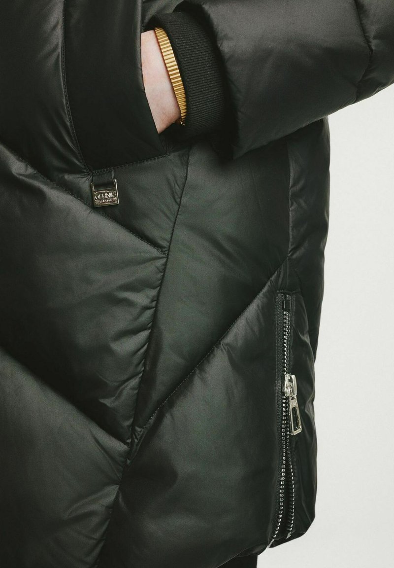 Schwarze Daunenjacke mit matter Oberfläche, diagonaler Steppung, einer Reißverschlusstasche und geripptem Bündchen. Mit einem metallischen Markenetikett.