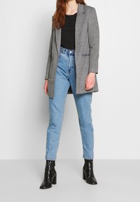 Szary, dopasowany żakiet noszony na czarnej bluzce, zestawiony z jasnoniebieskimi dżinsami i czarnymi, błyszczącymi botkami do kostek. Żakiet ma wycięty kołnierz i boczne kieszenie.