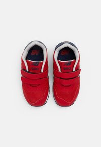 Chaussures en maille rouge et synthétique avec deux brides Velcro, doublure intérieure marine, et logo New Balance blanc sur le côté.