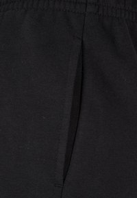 Černé tepláky vyrobené z měkké tkaniny, s elastickým páskem a boční kapsou se skrytým zipem.