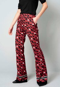 Uitlopende broek van een rode stof met een geometrisch zwart-wit patroon. Bevat zijzakken en een contrasterende zwart-wit zoom.