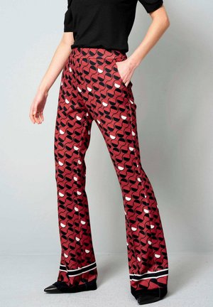 Uitlopende broek van een rode stof met een geometrisch zwart-wit patroon. Bevat zijzakken en een contrasterende zwart-wit zoom.