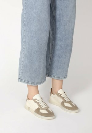 Weiße und beige Sneaker mit Wildlederelementen, runder Zehenform und strukturiertem Gummisohle, kombiniert mit hochgeschnittenen hellblauen Jeans.