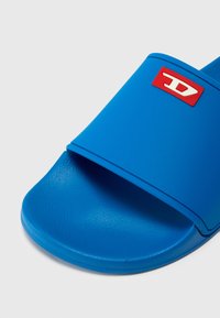 Modra drsna sandal z teksturirano podlogo, širokim pasom in rdečim logotipom. Narejena iz trajnega sintetičnega materiala.