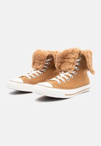 Sneakers alte in suede marrone con un morbido colletto in pelliccia sintetica, punta in gomma bianca e lacci. Presentano una suola bianca testurizzata con accenti marroni.
