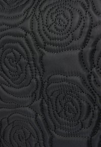 Tissu matelassé noir avec un motif de rose embossé, affichant une texture lisse et des détails de couture contrastants dans le design.