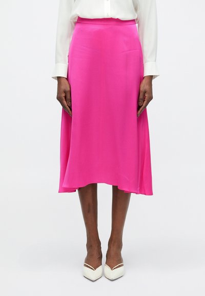 Jupe midi en soie rose avec une texture douce et fluide, dotée d'une taille lisse et d'une légère forme évasée. Assortie à des talons blancs.