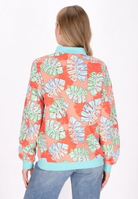 Giacca bomber colorata realizzata in tessuto leggero, con uno sfondo corallo e grandi motivi a foglia in verde, blu e bianco.