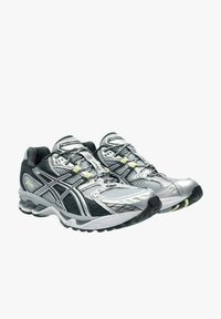 Scarpe sportive argento e nere con tomaia in mesh, finitura testurizzata, sistema di allacciatura prominente e suola in gomma a contrasto con accenti gialli.