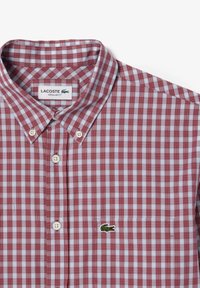 Camisa de cuadros en rojo y azul con cuello, que presenta botones de perla y un logotipo bordado en verde en el bolsillo del pecho izquierdo.