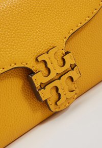 Bolso de mano de cuero amarillo con una superficie texturizada y un distintivo cierre de logotipo de hardware oscuro. Cerrado con un detalle de costura contrastante.